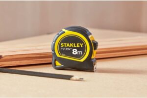Mètre ruban Stanley 8 mètres posé sur établi, accessoire indispensable pour les mesures fiables à la maison comme sur chantier. mètre ruban 8m