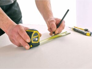 Mètre ruban Stanley 8 m en action pour mesurer une planche, idéal pour les travaux de bricolage et d’aménagement intérieur.